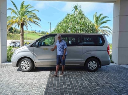 A taxi driver is standing holding the door to the passenger seat.