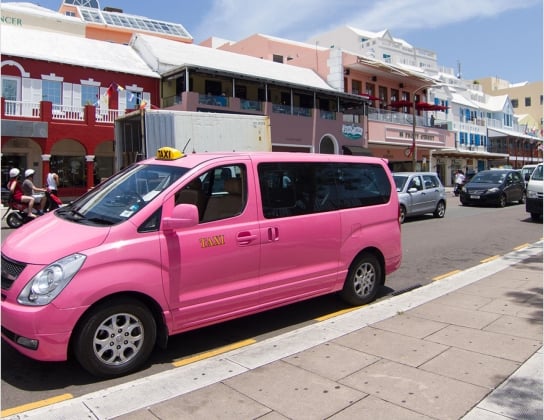 A pink taxi van parked on the side of a road.