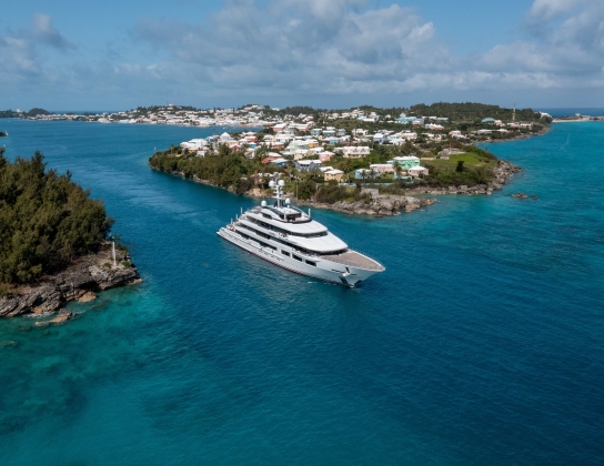 A large super yacht is exiting the channel on calm blue waters.