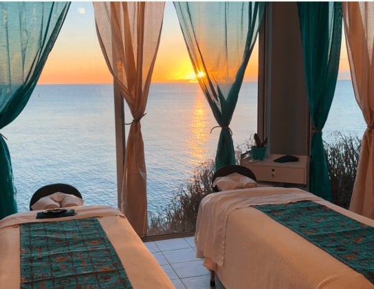 Two massage beds under a gazebo with a sunset with calm waters in the background.