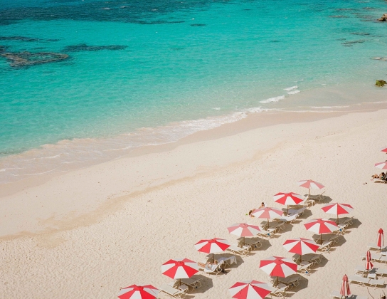 An aerial view of a beautiful pristine beach with red and white umbrellas.
