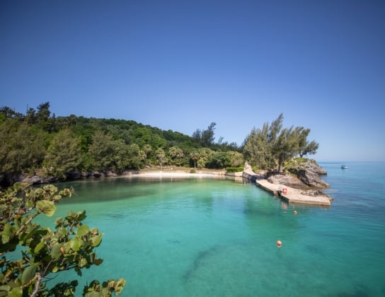 a view of a nearly empty pristine beach with calm waters and a boat in the distance.