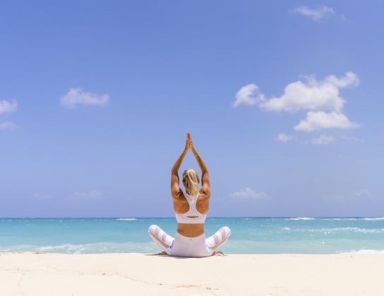 A woman is posing doing yoga on the beach.