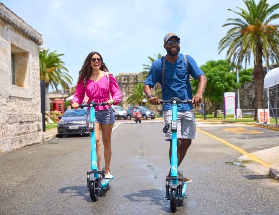 A man and a woman are riding electric scooters.