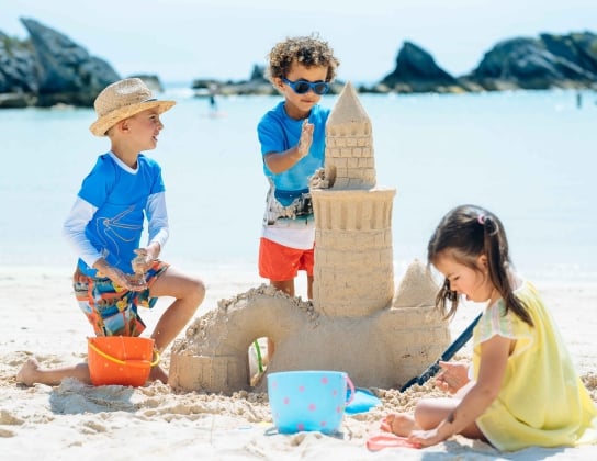 A group of kids are playing in the sand at the Hamilton Princess Beach Club