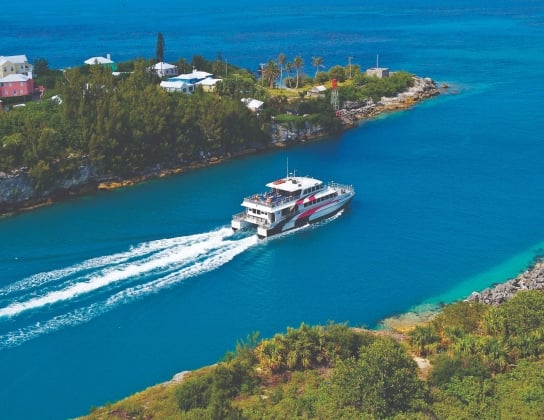 A ferry is riding out of St. George's with calm blue waters.