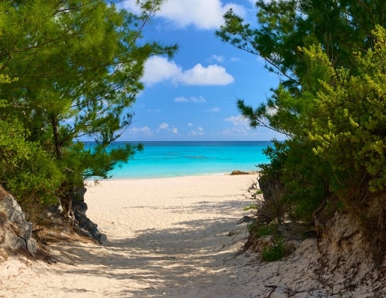 A view of an empty beach with clouds and clear blue waters.