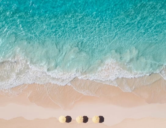 An aerial view of three yellow beach umbrellas in sand by the water.