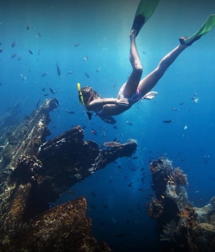 snorkelers diving down by coral structures 