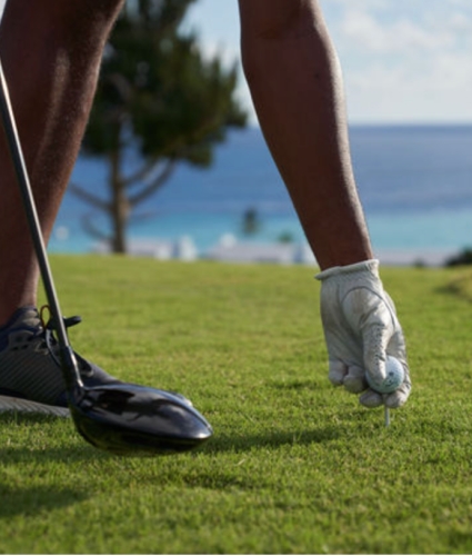 A man playing golf in Bermuda, placing a tee on the ground.