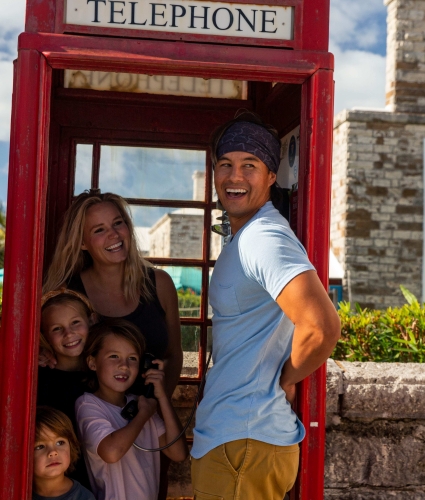 A family is piled up in an old style British telephone booth smiling at something in the distance.