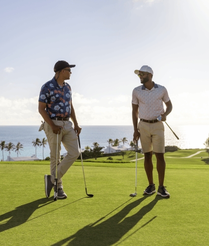 Two men are standing on a golf course talking. 
