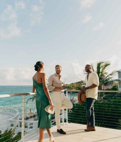 A woman and two men are standing on a balcony laughing. 