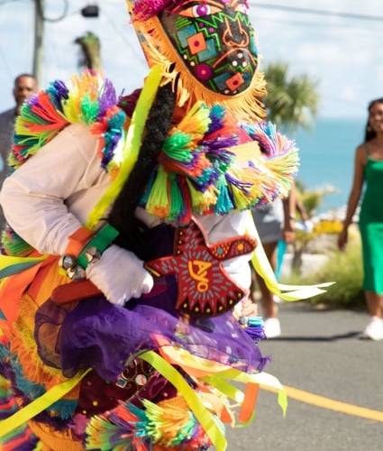 A close up of a gombey dancer with people dancing and walking behind.