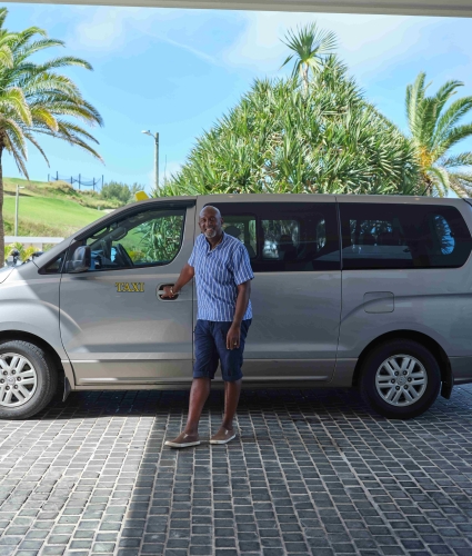 A taxi driver is standing holding the door to the passenger seat.