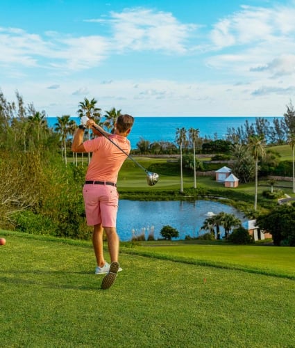 A man is teeing off on a scenic course with the ocean in the background.