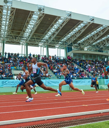 A group of runners are run on a track with a crowd watching in the back.