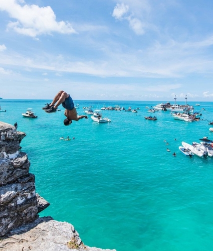 A person doing a backflip off a rock into the sparkling blue waters of Bermuda