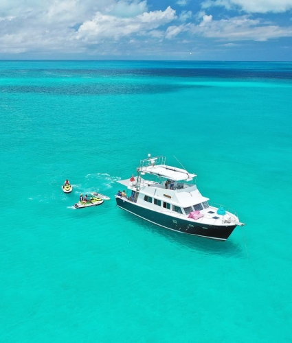 A boat on turquoise water near people on sea-doos 