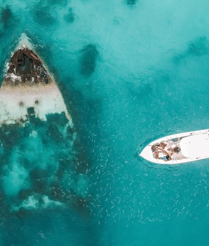 A boat approaches a Bermuda shipwreck visible through the clear, turquoise waters.