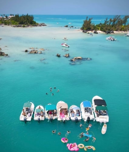 A line of boats in blue water with people swimming around them