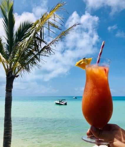 A hand holding a tropical drink up in front of the ocean