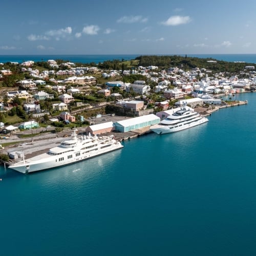 Aerial view of dock with two superyachts and calm blue waters.
