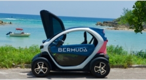 An electric car parked on the road next to the ocean.
