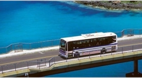 A city bus drives down an bridged road crossing the ocean.