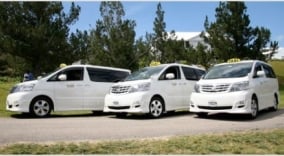 Three white taxi vans parked in a parking lot.