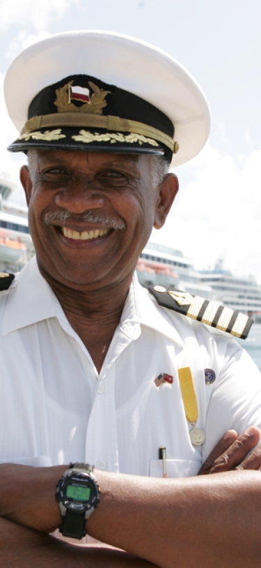 A boat pilot is smiling at the camera with three cruise ships behind him.