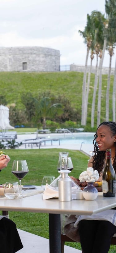 Two women are sitting eating dinner with a fort in the background.