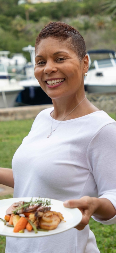 A waitress is smiling at the camera with three plates in her hands.