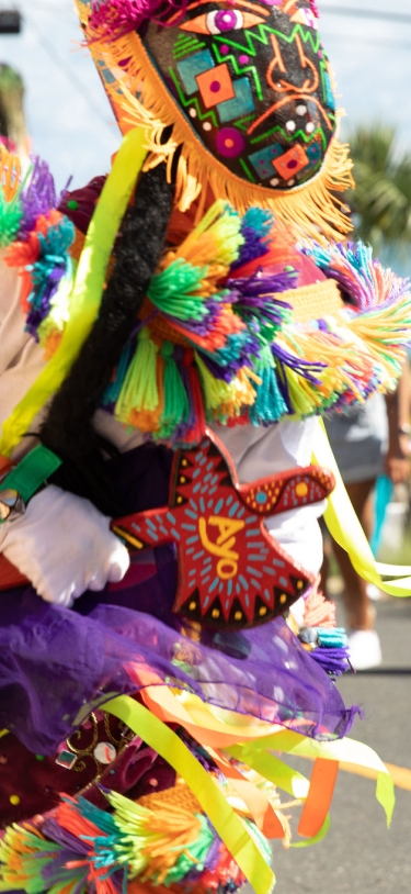 A close up of a gombey dancer with people dancing and walking behind.
