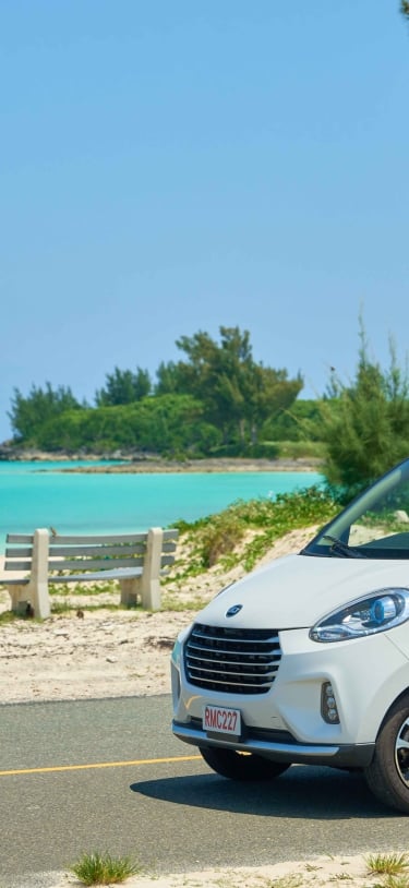 A woman is driving a micro car with a beach in the background.