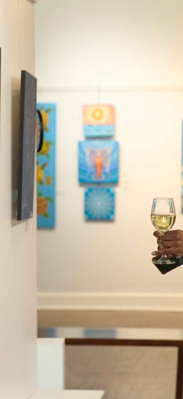 A woman is holding a glass of wine staring at art on a wall