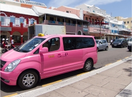 A pink taxi van parked on the side of a road.