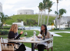 Two women are sitting eating dinner with a fort in the background.