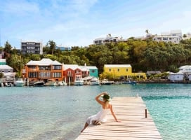 A woman is sitting on a dock looking out a colourful buildings.