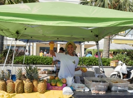 A woman is smiling at the camera at her food stand.