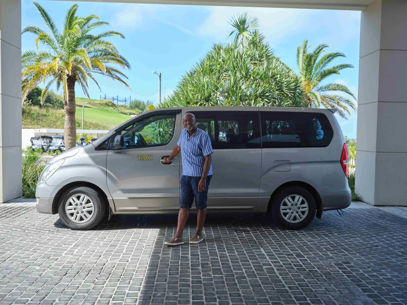 A taxi driver is standing holding the door to the passenger seat.