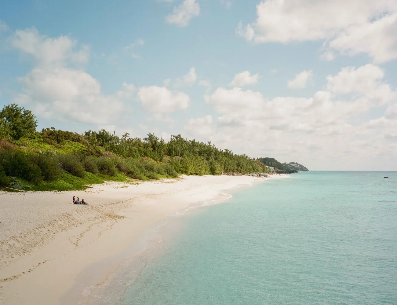 A wide shot of a small group of people sitting on a vacant pristine beach. 