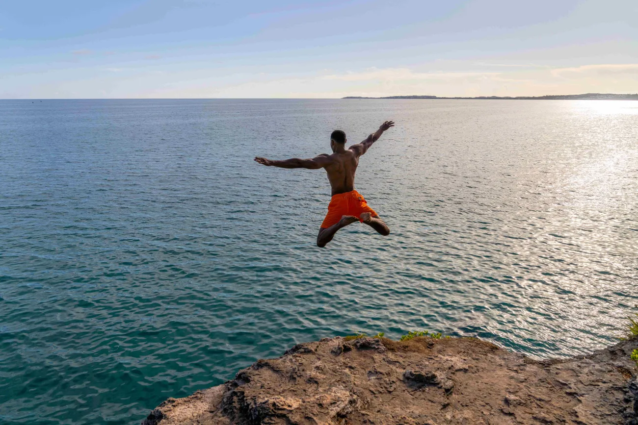 A man is star jumping into the ocean from a cliff.
