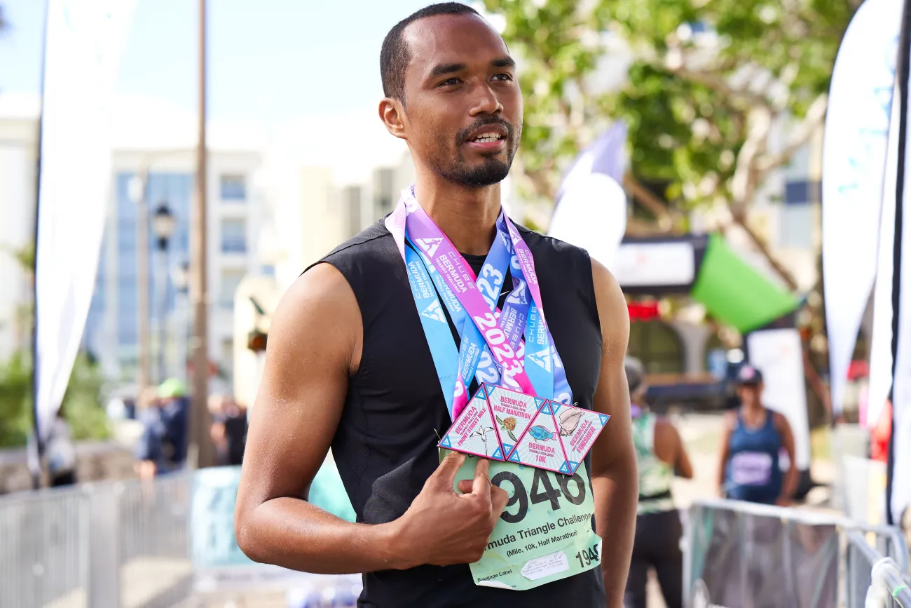 A man is standing holding four medals during the Chubb Triangle Challenge.
