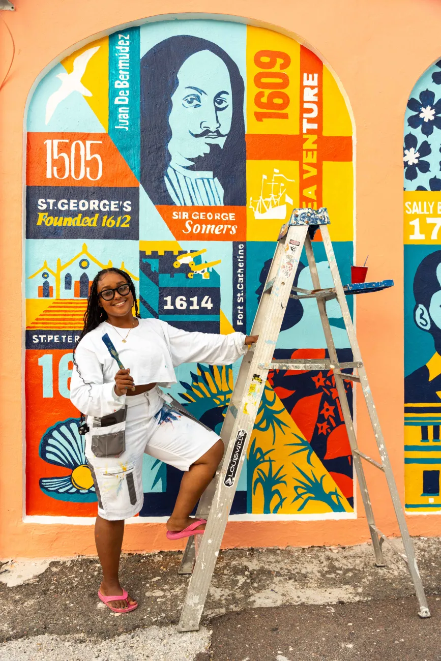 A woman is smiling at the camera with paint brushes.
