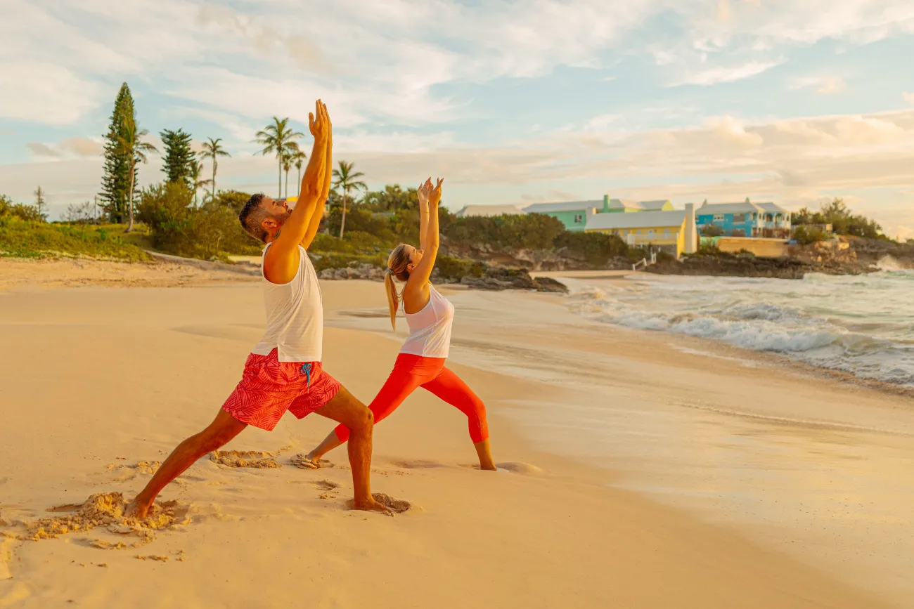 A couple is doing yoga on the beach at sunset.