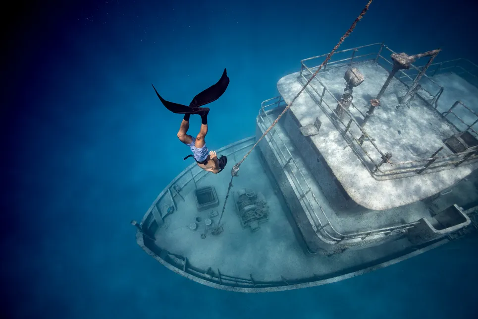 A man free diving in clear waters near sunken shipwreck.