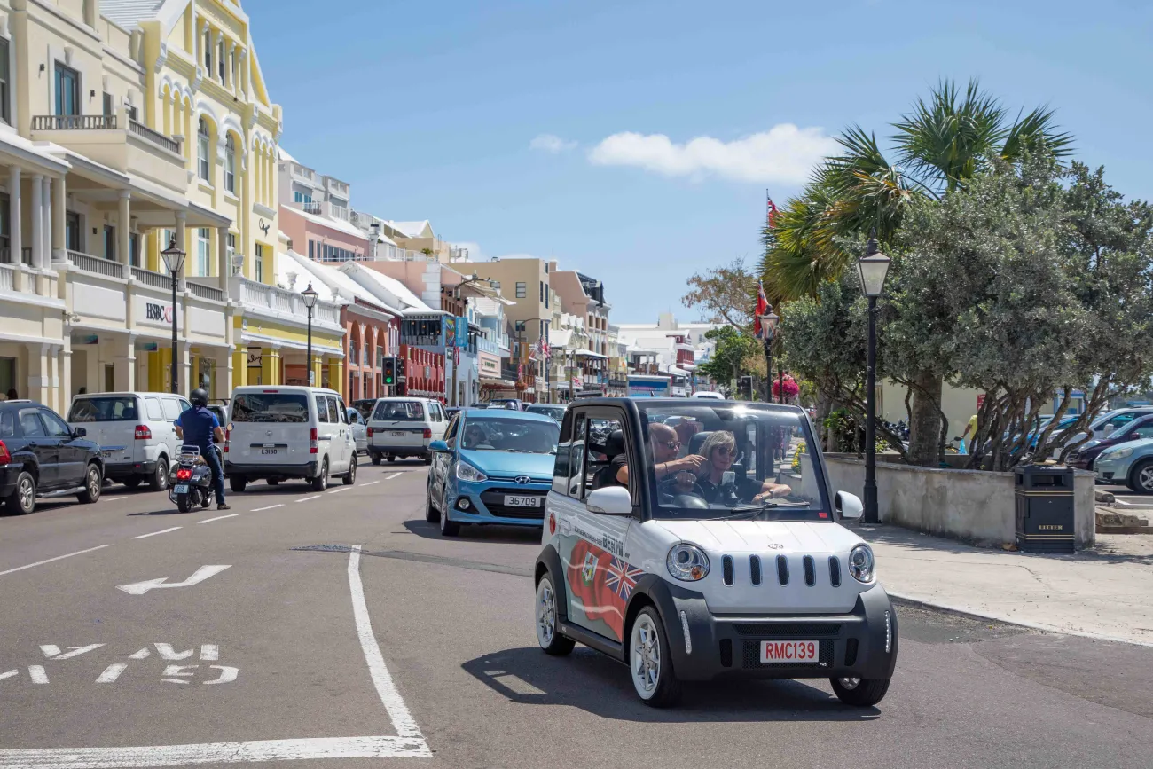 A couple is driving on front street in a microcar.