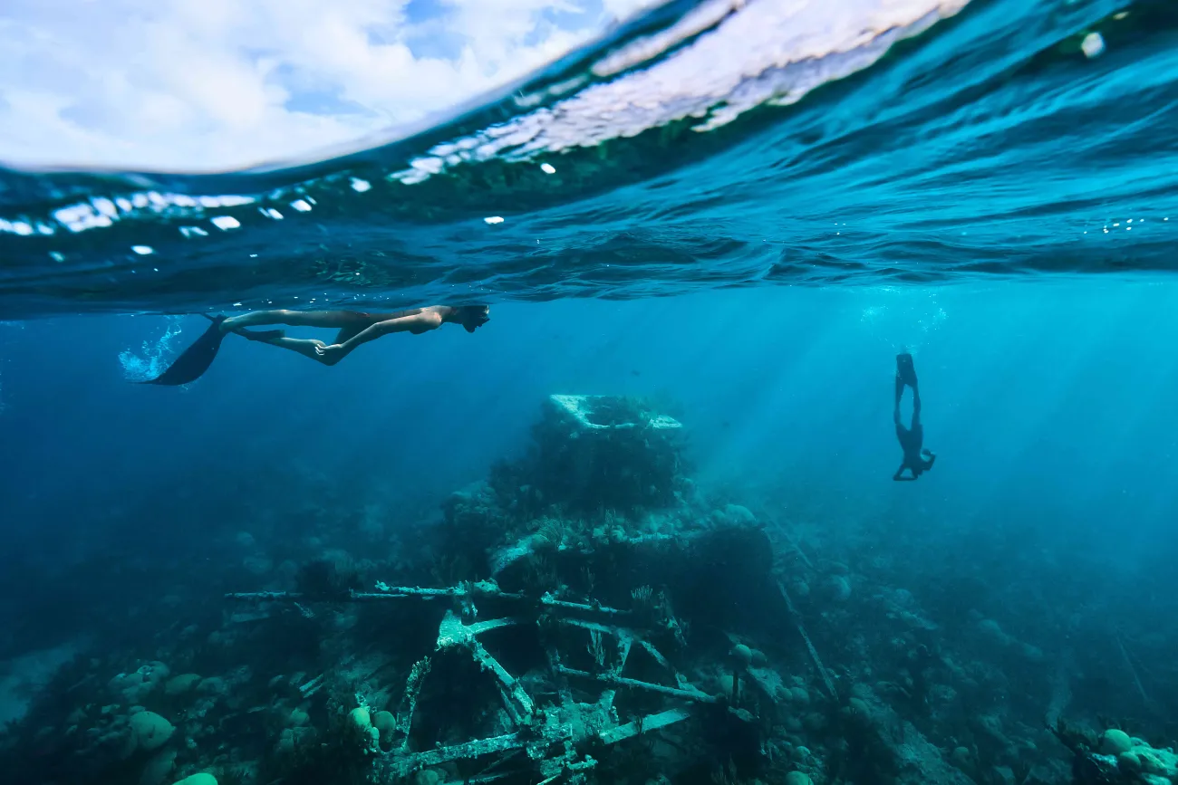 Two people are snorkeling in clear water around a shipwreck.