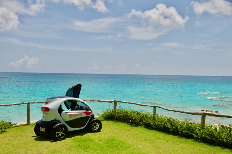 A twizy is on the grass by the calm blue ocean.